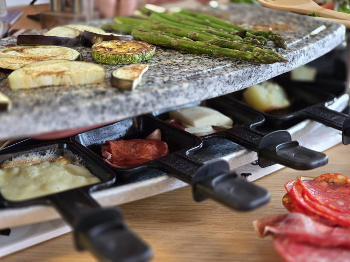 raclette grill with food on top and cheese melting in pans